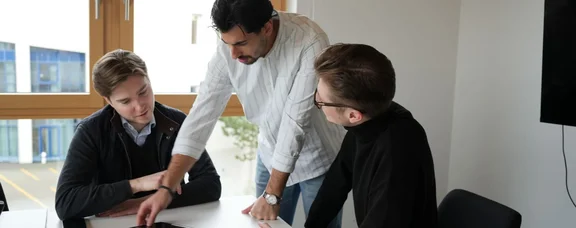 An der UW/H erhalten junge Menschen die Werkzeuge, um erfolgreich zu gründen. (Foto: UW/H) Drei Studierende sitzen zusammen an einem Konferenztisch und schauen gemeinsam auf ein Tablet.