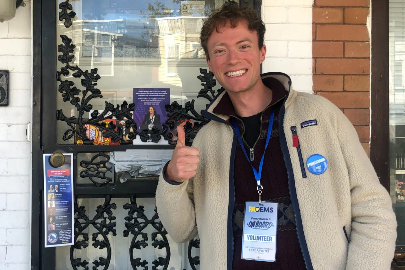 Eine Person zeigt den Daumen hoch vor einer Haustür mit Wahlkampfmaterial.