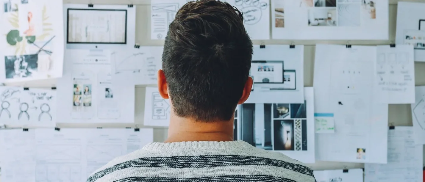 Der Kurs unterstützt Wissenschaftler:innen dabei, ihre Forschungsprojekte zu organisieren. (Foto: pexels) Ein Mann steht mit dem Rücken zur Kamera und betrachtet Papiere, die an der Wand angebracht sind.