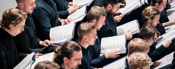 The University Choir of the UW/H (Photo: UW/H │ Daniela Arndt) Close-up of a university choir. All the singers are holding sheet music and song lyrics in their hands.