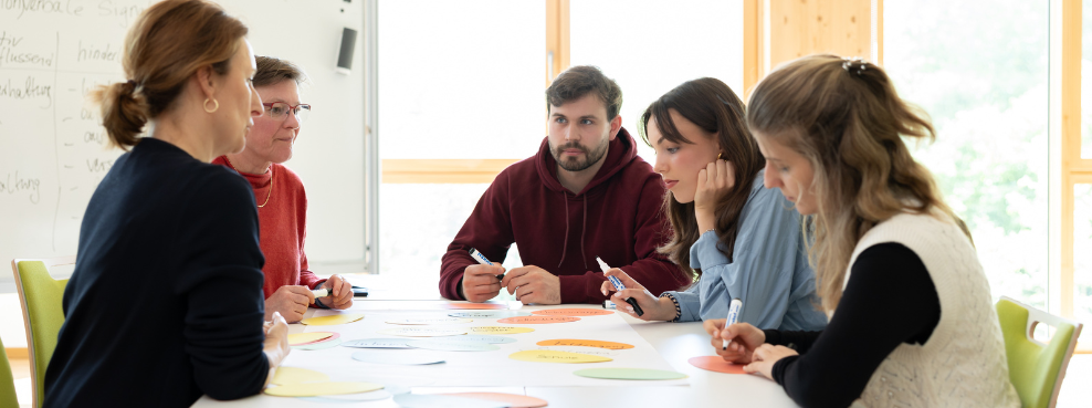 Five people sit at a table and write keywords on colourful cards.