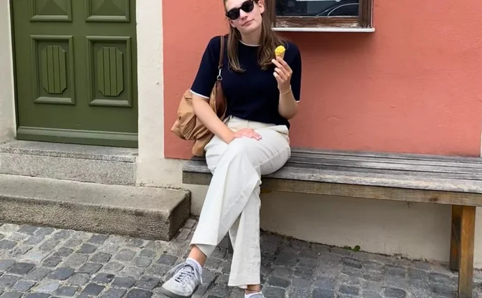 Pia Klee sitzt auf einer Holzbank vor einer roten Hauswand und isst ein Eis.