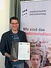 A man with a certificate in his hand smiles at the camera.