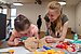 A girl examines a teddy bear together with a student.