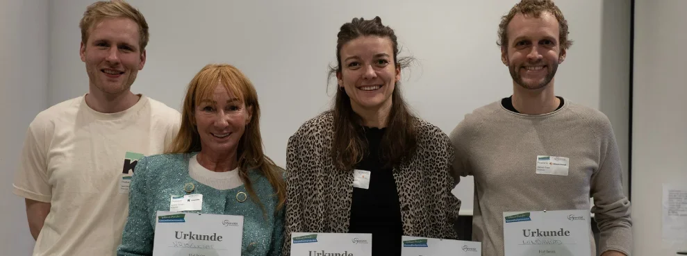 Vier Personen stehen nebeneinander und halten eine Urkunde in die Kamera.