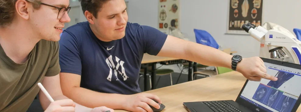 Zwei Studenten sitzen an einem Laptop.