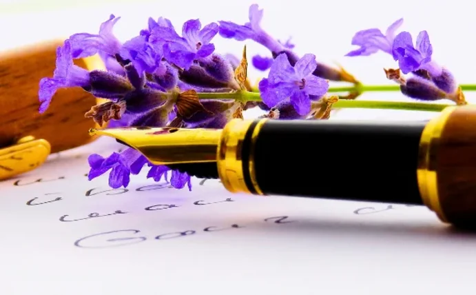 Man sieht einen edlen Füller vor einem weißen Hintergrund mit einer lila Blume. 