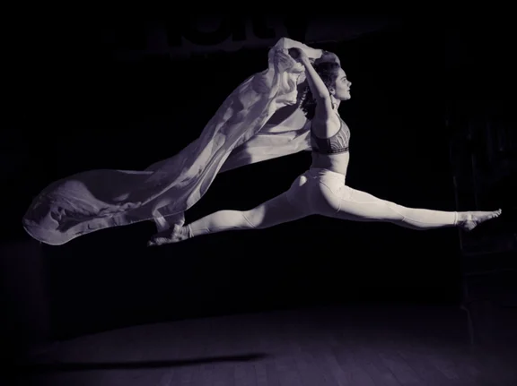 Schwarzweiß-Aufnahme einer Tänzerin, die in der Luft einen Spagat macht.