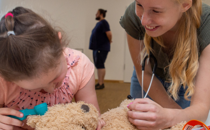 Ein Mädchen untersucht zusammen mit einer Studentin einen Teddybären.