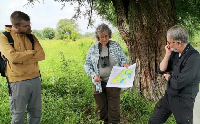 Drei Personen stehen in der Natur und schauen auf eine Karte, die die Frau in der Mitte in der Hand hält.