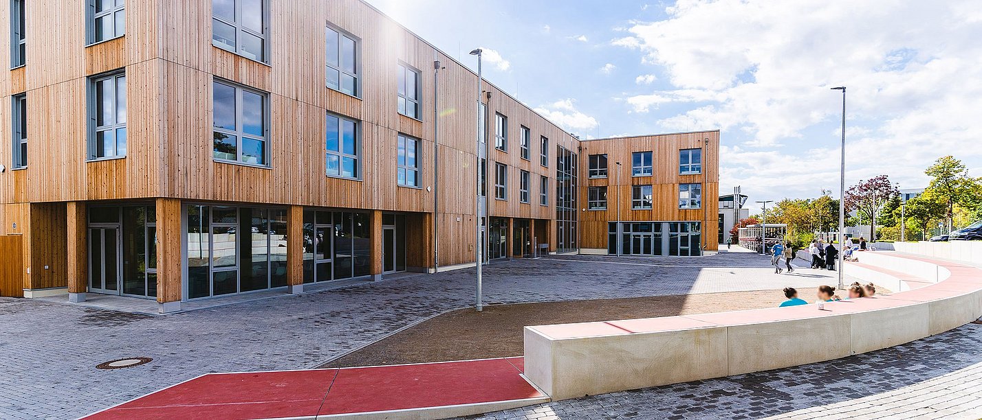 Der Holzbau der Uni Witten/Herdecke: Fast komplett aus nachwachsenden Rohstoffen gebaut (Foto: UW/H | Johannes Buldmann) Bild eines Holzgebäudes mit Vorplatz in der Sonne
