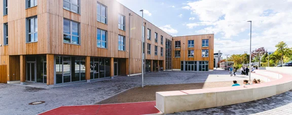 Bild eines Holzgebäudes mit Vorplatz in der Sonne