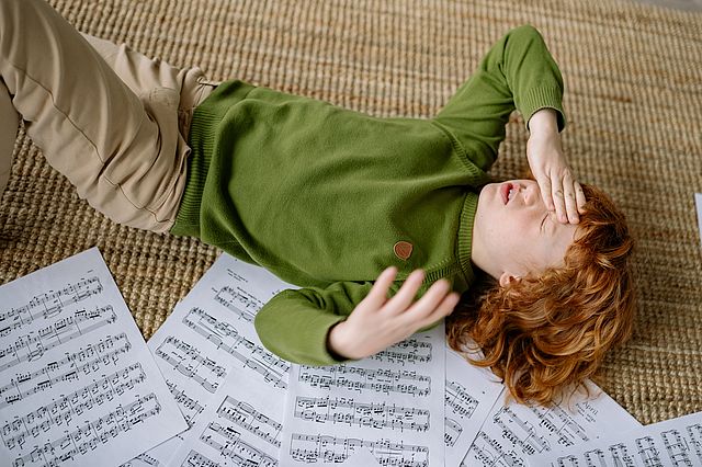Kind liegt mit Kopfschmerzen auf Notenblättern