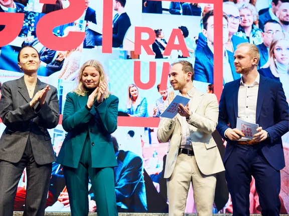 Vier Studierende stehen auf einer Bühne und klatschen.