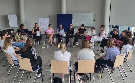 A circle of chairs with several workshop participants in a bright room.