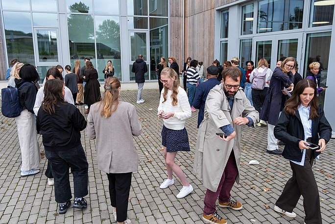 One highlight was the artistic contribution "Tunnel Bingo" by Julie C. Stamm (Resident Kulturforum Witten), which was created in cooperation with Dr Regine Ehleiter from WittenLab. (Photo: UW/H | Klara Schmickler)  Several people walk across a square and look at their smartphones.