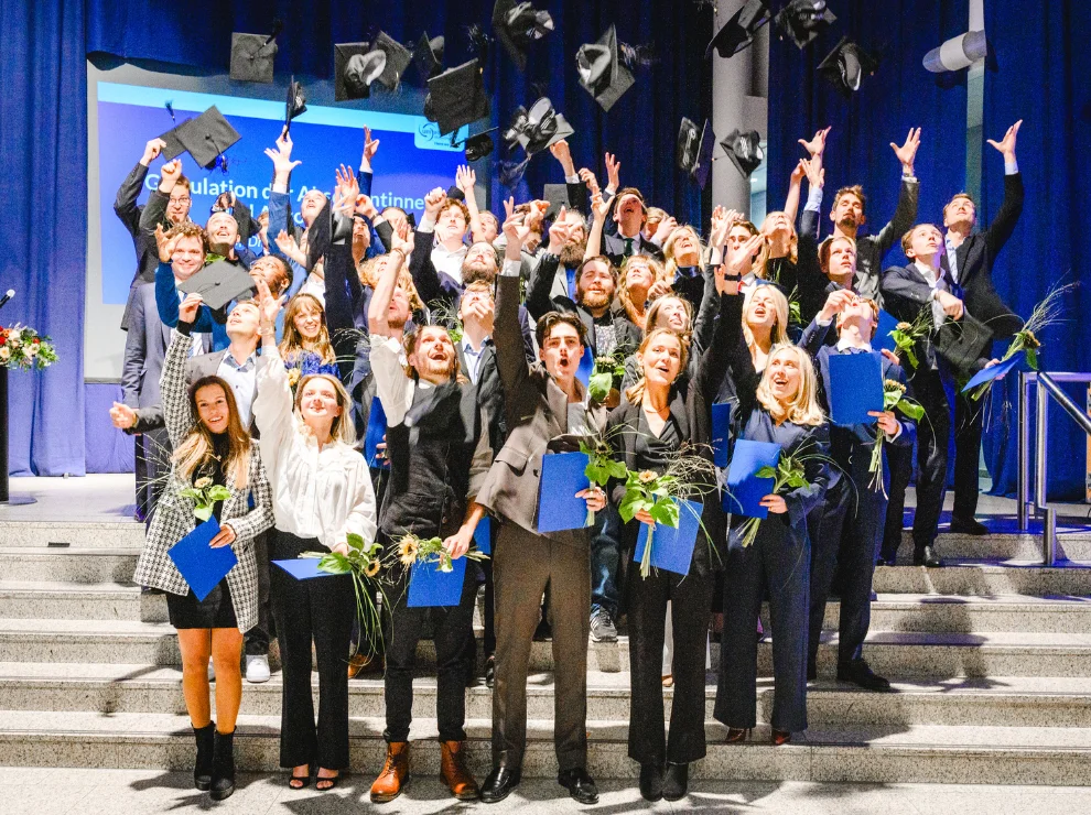 Gruppenfoto von Absolvent:innen, die ihre Hüte in die Luft werfen.