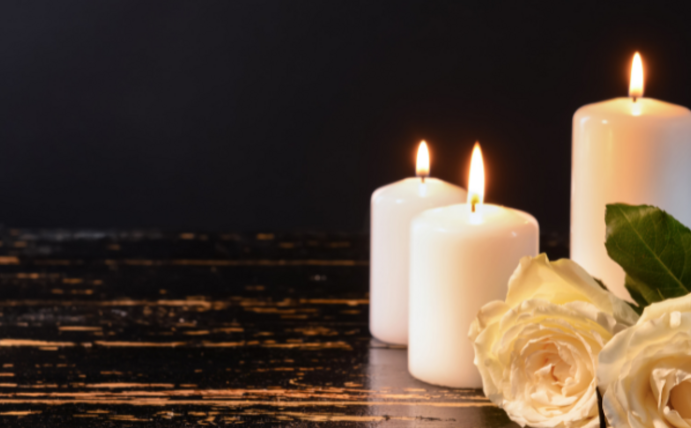 Drei angezündete Kerzen und zwei weiße Rosen vor dunklem Hintergrund