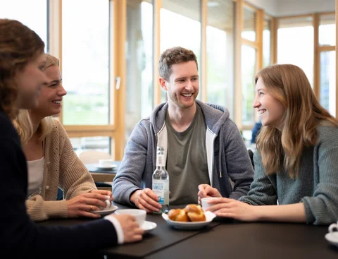 Café Larix (Photo: UW/H | Michael Schwettmann) A group of students are drinking coffee together. Drinks and pastries are placed in front of them.