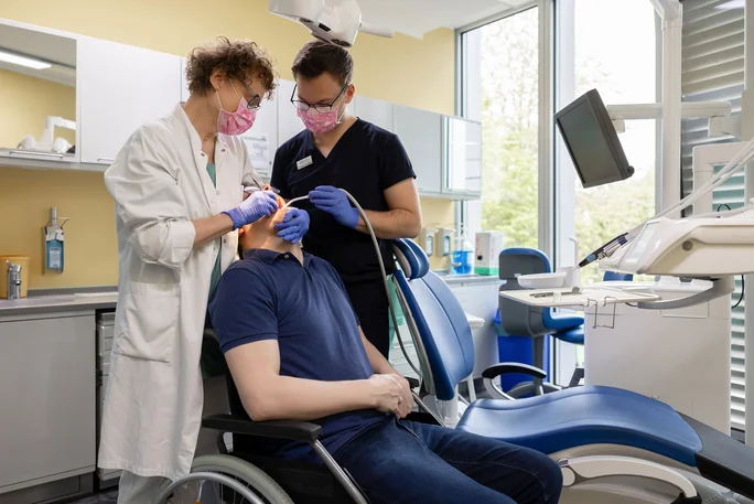 A student and a dentist treat a man in his wheelchair
