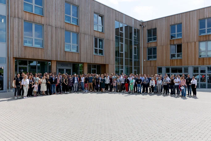 Alumnae and alumni gather for a group photo on the UW/H campus (Photo: UW/H | Michael Schwettmann) A large group of people are posing in front of a wooden building.