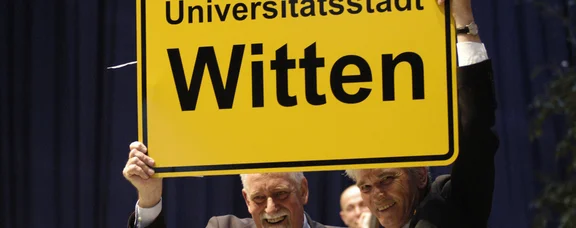 Mann hält Ortsschild von Witten hoch: Universitätsstadt Witten