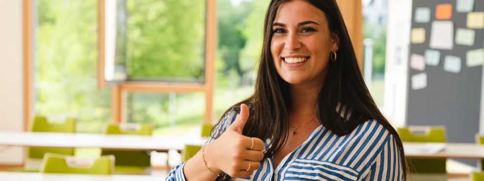 Eine Studentin lächelt in die Kamera und zeigt einen Daumen hoch.