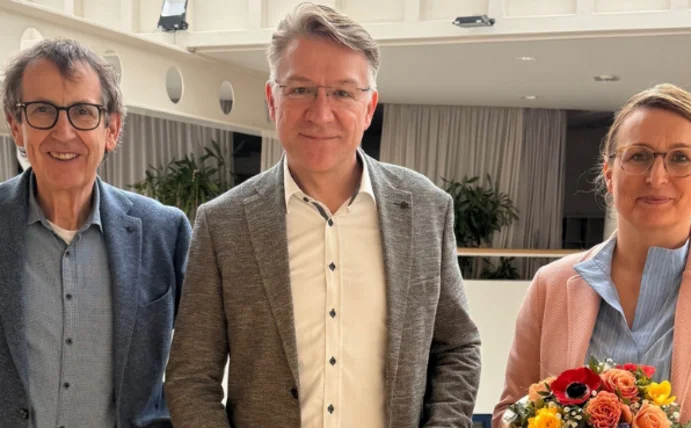 Drei Menschen stehen im Hauptgebäude der Uni W/H. In der Mitte steht Prof. Dr. Dr. Lars Bonitz, der mit einem Lächeln seine Berufungsurkunde in der Hand hält.