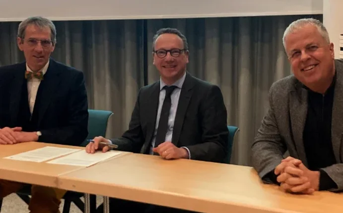 Drei Personen sitzen nebeneinander an einem Tisch und lächeln in die Kamera.