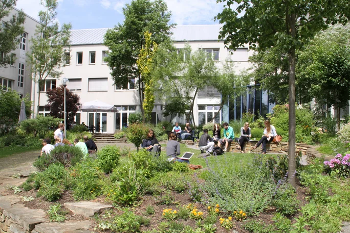 Außenbereich vor der Cafeteria im Hauptgebäude, Studierende sitzen im Garten