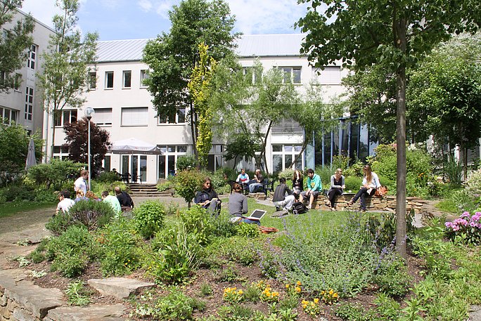 Außenbereich vor der Cafeteria im Hauptgebäude, Studierende sitzen im Garten