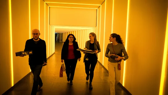 Vier Personen laufen einen Gang mit gelblichem Licht entlang.
