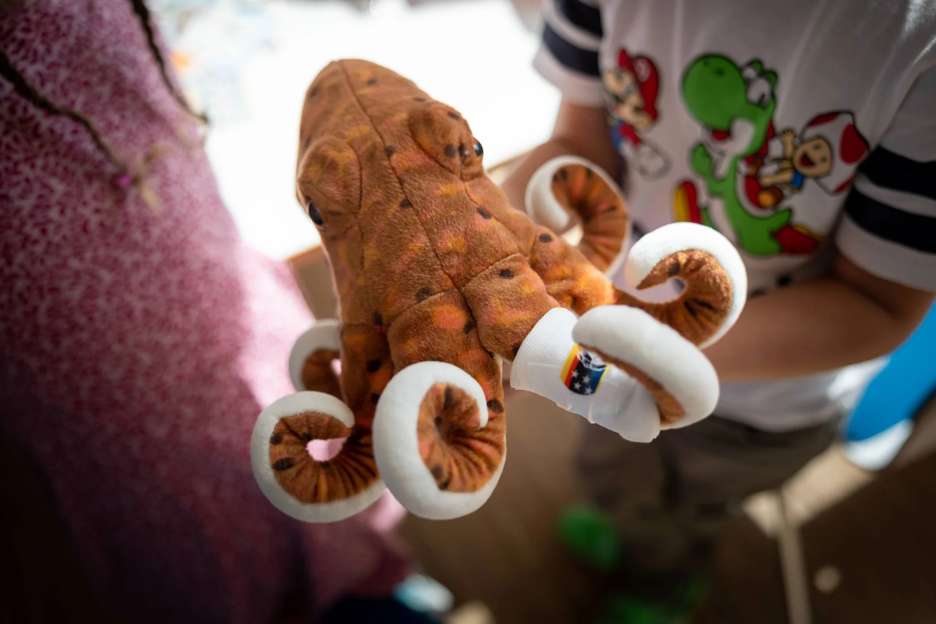 KiTa an der UW/H. (Foto: UW/H | Michael Schwettmann) Im Fokus steht ein brauner Plüsch-OKtopus. Im Hintergrund sind Kinder zu erkennen, die mit ihm spielen.