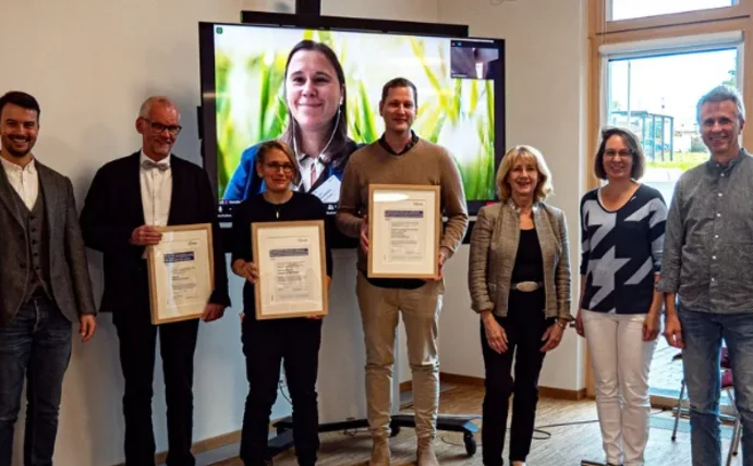 Gruppenfoto, drei Menschen in der Mitte halten eine Urkunde in die Kamera.