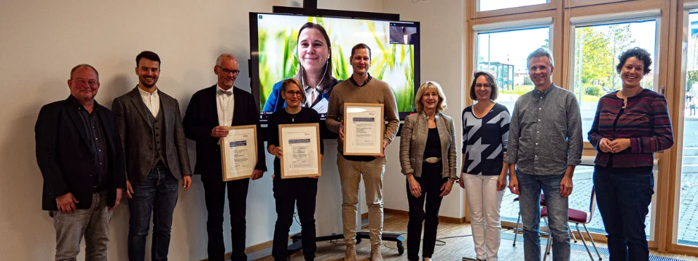 Group photo, three people in the centre holding a certificate up to the camera.