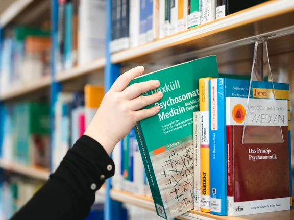 Person greift ein Buch aus dem Regel
