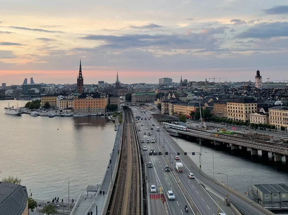 Blick auf die Skyline von Stockholm in der Abenddämmerung. Im Vordergrund ist eine Straßenbrücke, die über einen Fluss führt.