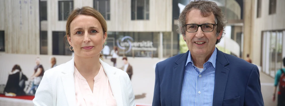 Eine Frau und ein Mann stehen nebeneinander und lächeln in die Kamera.