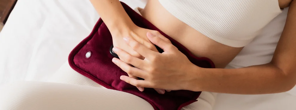 You can see a woman's belly covered with a hot water bottle. She suffers from endometriosis pain.
