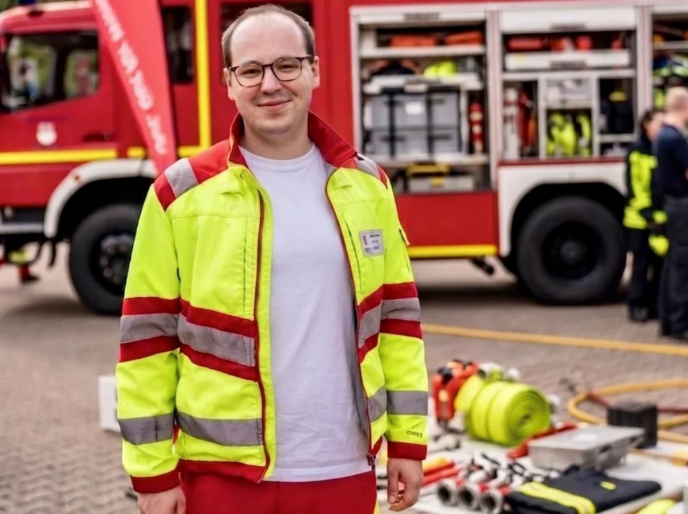 Porträt von Tim Schröder vor einem Einsatzwagen der Feuerwehr.
