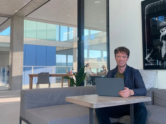 Victor Wolff sitzt mit seinem Laptop an einer Tischecke zum Lernen. Im Hintergrund sieht man Innenräume der Universität St. Gallen.