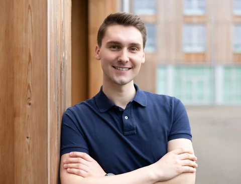 Bewirb dich für den Modellstudiengang Medizin (StEx) an der UW/H. (Foto: UW/H | Michael Schwettmann) Ein junger Mann steht seitlich gelehnt an einer Gebäudewand aus Holz.