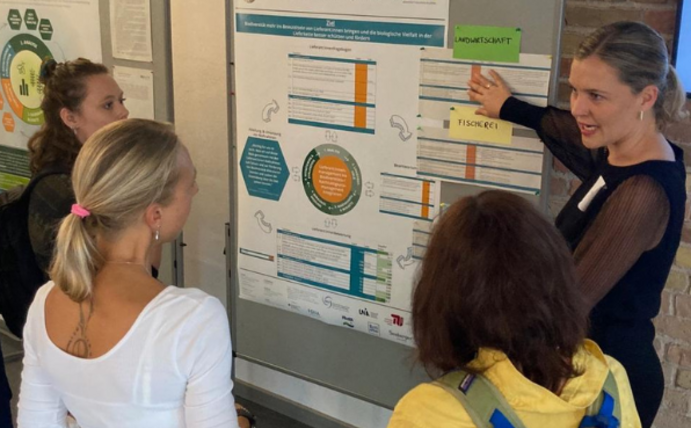 Die Diskussionsstation "Biodiversität managen": Dr. Verena Timmer, ZNU, im Gespräch mit Teilnehmenden. (Foto: BioVal) Teilnehmende stehen vor einer Metaplanwand mit einem Poster und sprechen mit Verena Timmer vom ZNU.