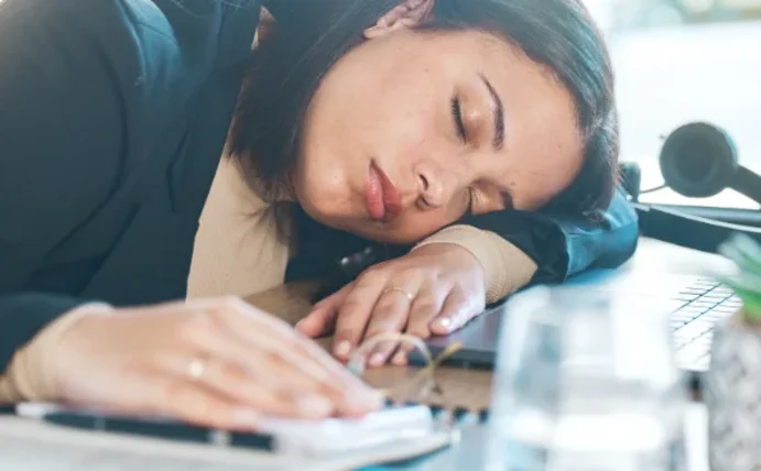 Eine neue Leitlinie zu Narkolepsie bietet Handlungsempfehlungen für Mediziner:innen und bessere Therapiemöglichkeiten für Betroffene (Foto: Canva). Das Foto zeigt eine schlafende Frau, die ihren Kopf vor dem Notebook auf den Schreibtisch abgelegt hat.