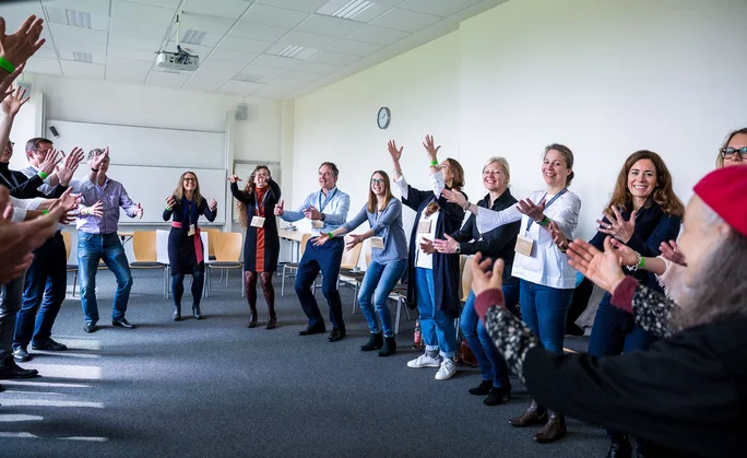 Eine Gruppe von Menschen steht in einem Kreis und hebt die Hände zur La Ola-Welle.