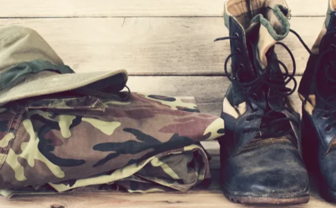 Man sieht die Kleidung eines Soldaten. Eine gefaltete Hose in Tarnfarben, Stiefel und einen Hut.