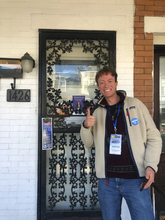 Bild von einem jungen Mann, der vor Wahlwerbung für Kamala Harris den Daumen in die Luft reckt.