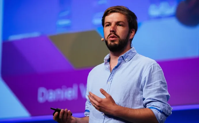 Daniel Verst steht auf einer Bühne und hält einen Vortrag.