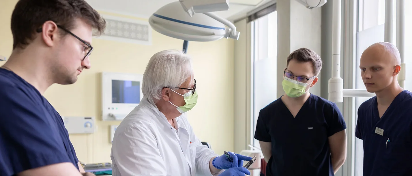 Ein Zahnmedizin-Professor erklärt drei Studierenden ein Gerät.