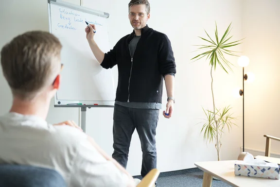 Ein Therapeut und ein Patient in einer Gesprächssituation, der Therapeut schreibt Ergebnisse auf ein Flipchart.